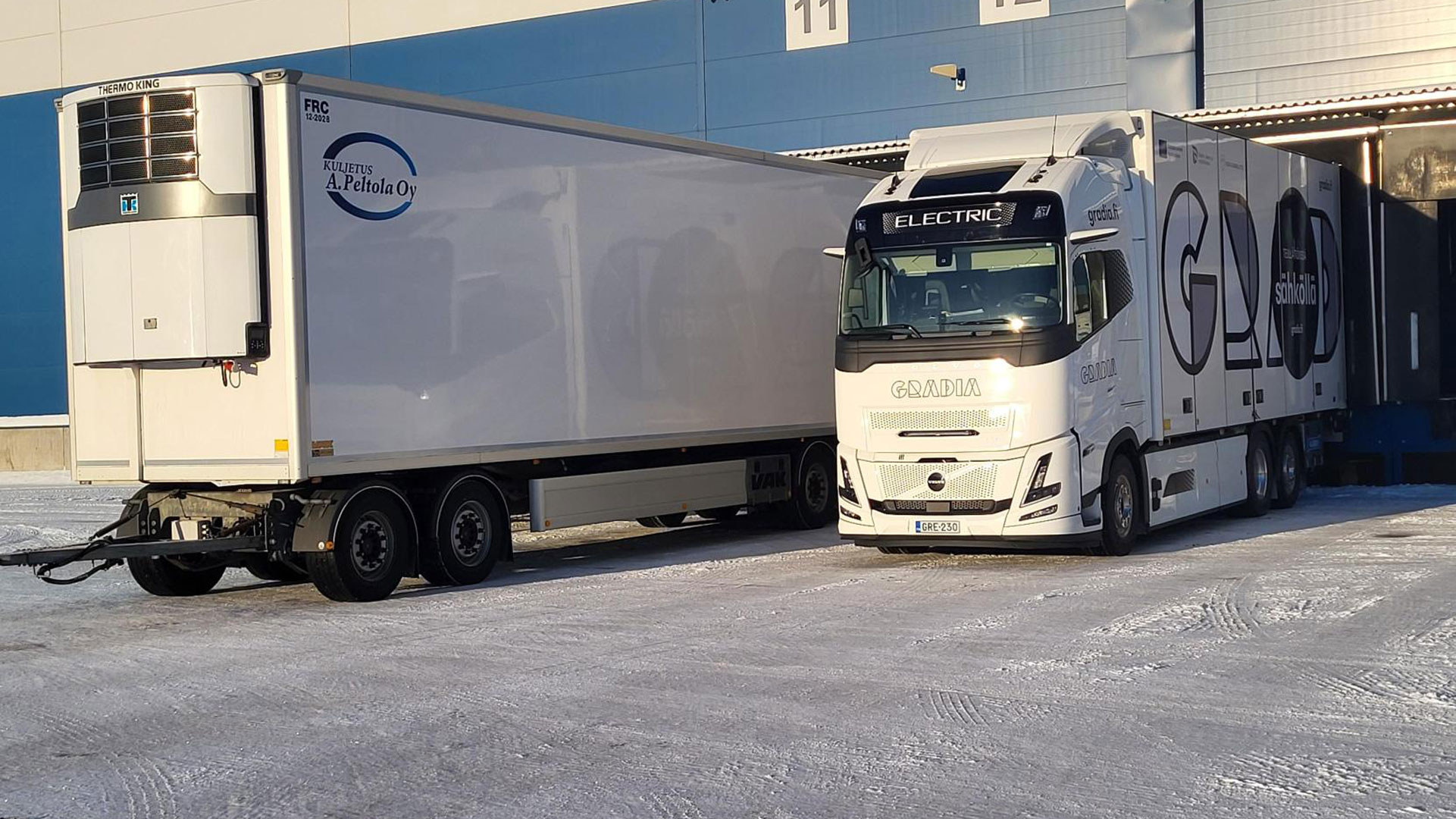 Gradian sähkökuoma-auto ja Peltolan perävaunu rinnakkain terminaalilla aurinkoisena talvipäivänä.