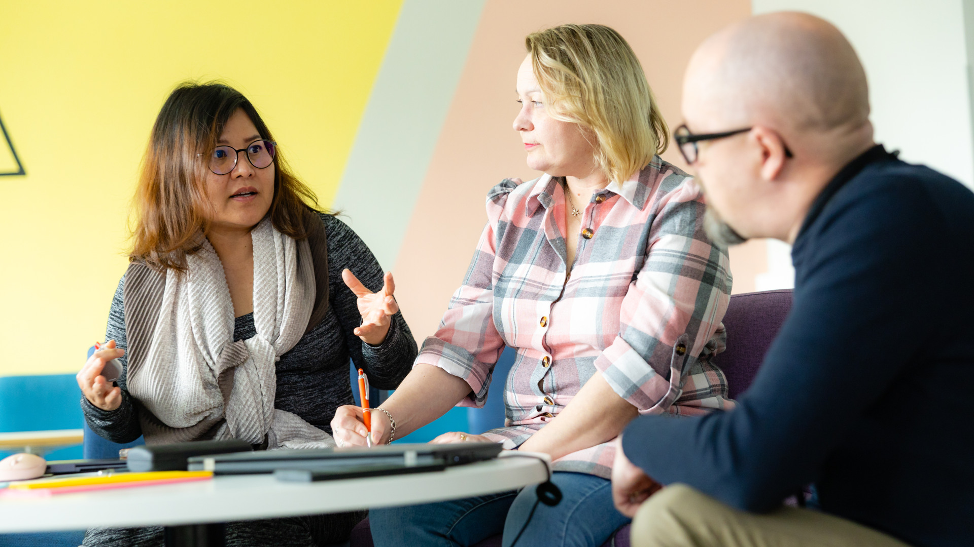 Anne Liimatainen istuu opiskelukaverin sekä opettajan kanssa luokassa ja keskustelevat tehtävästä.