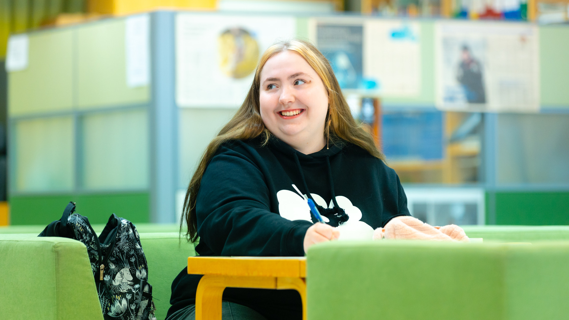 Nainen istuu pöydän äärellä kynä kädessään.