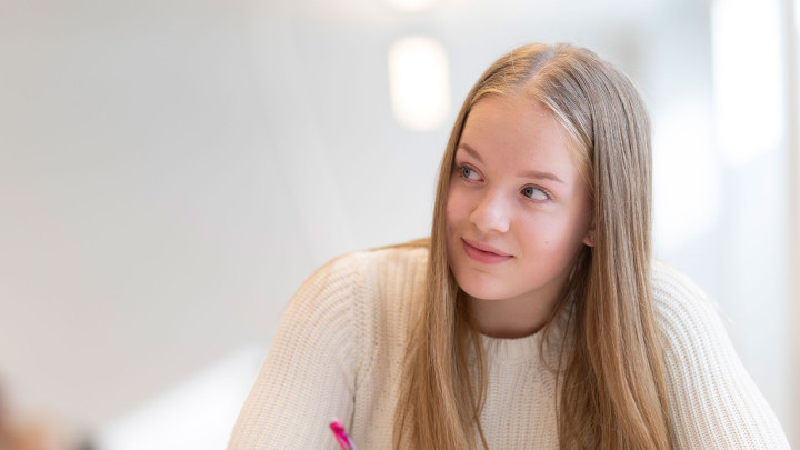 Lukiolaistyttö istuu miettiväisen näköisenä.