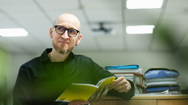 Opettaja Jarkko Sairanen oppilaitoksen tiloissa kirja kädessään.