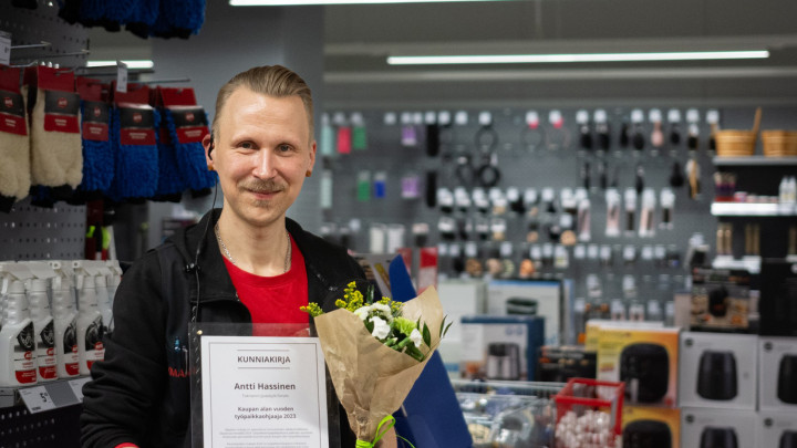 Antti Hassinen työympäristössään myymälässä palkinnostaan saama todistus kädessään.