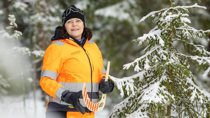 Riitta Kosonen talvisessa metsässä työvaatteissa katsoo kameraan.
