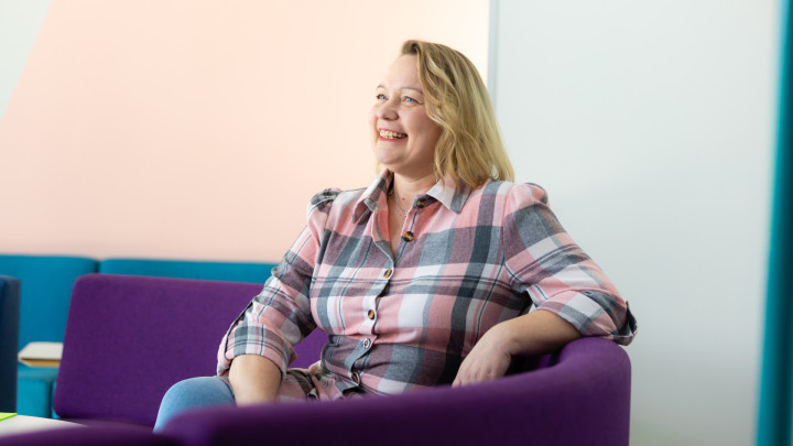 Liiketoiminnan ammattitutkinnon tutkinnon osan opiskelija Anne Miettinen istuu Gradian luokkahuoneen violetilla sohvalla hymyillen.
