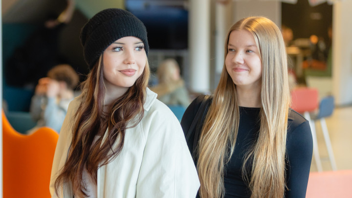 Kaksi nuorta naisopiskelijaa seisovat lukion aulassa.