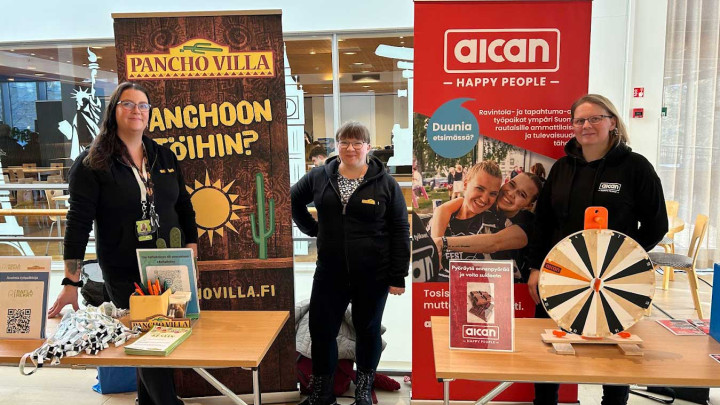Kuvassa kolme naista seisoo Gradian rekrytointitapahtumassa pöytien takana esittelemässä omien yritystensä (Pancho Villan ja Aican) avoimia työpaikkoja. Kuvassa kolme naista ja heidän takanaan yritysten roll-upit.